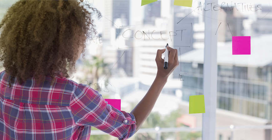 Woman writing ideas on dry erase board with colorful sticky notes.